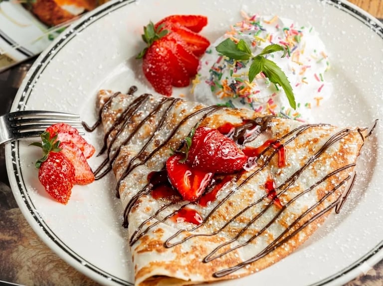 Plate of crepes drizzled with chocolate, topped with strawberries and whipped cream, served with colorful sprinkled frosting