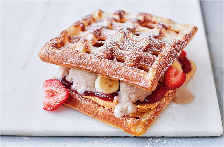 Waffle sandwich with strawberries, whipped cream, and powdered sugar on a white plate